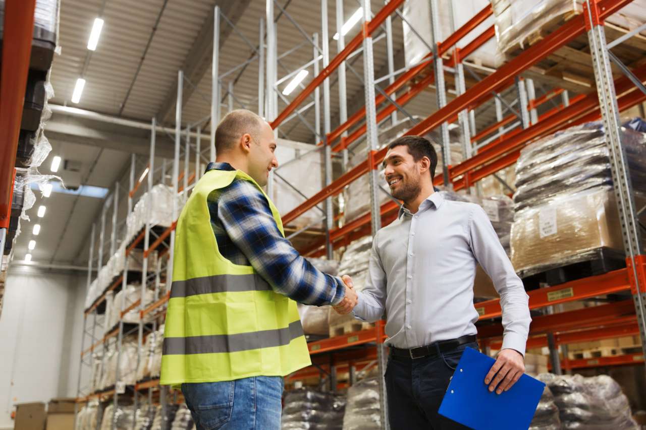 worker and businessmen with clipboard at warehouse two people shaking hands in a warehouse
