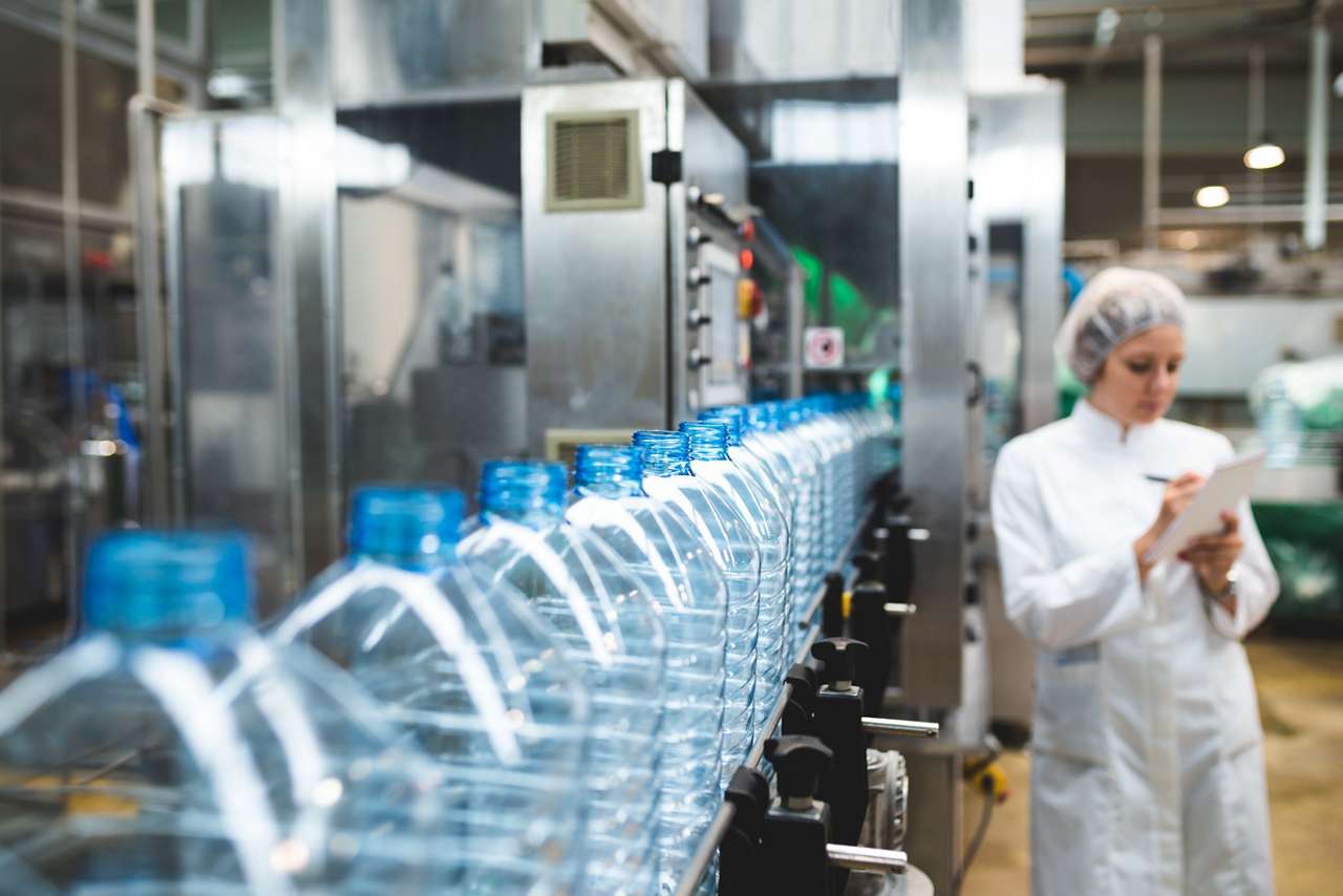 Young happy female worker in factory writing notes about water bottles or gallons before shipment. Inspection quality control. 