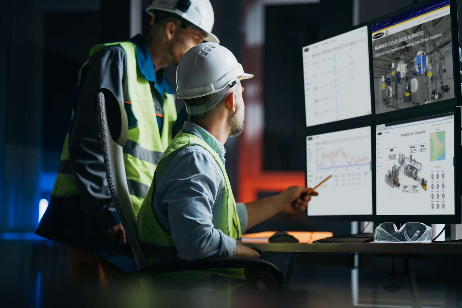 Two men in hardhats in front of multiple computer screens